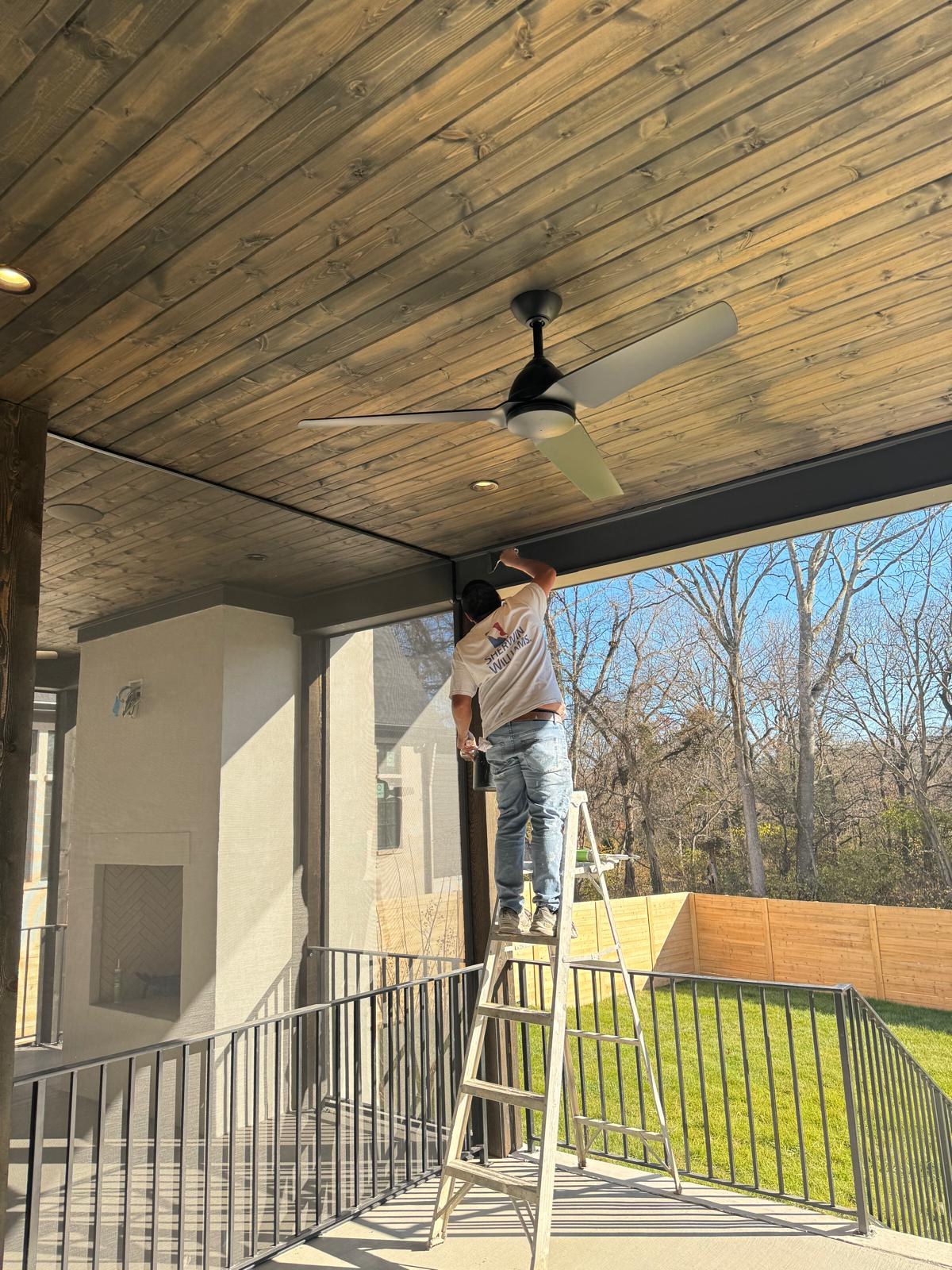 A painter working from a ladder on a covered porch ceiling