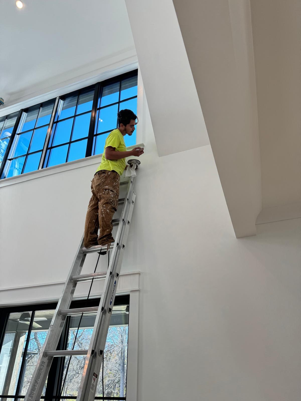 A painter on an extension ladder painting a tall interior wall