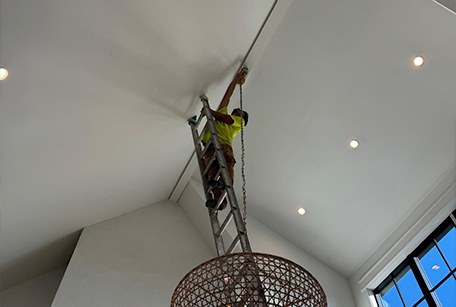 A painter on a tall ladder painting a high-ceilinged room